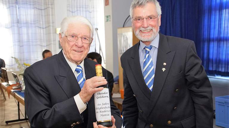 Theodor Gelshorn gehört seit 60 Jahren dem Ruderclub Hansa an.  Theodor Gelshorn hält eine Flasche in die Kamera. Daneben Ulrich Hahn.